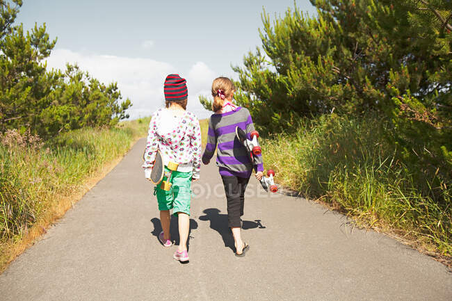 Girls carrying skateboards along rural road — Stock Photo