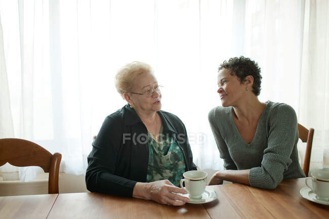 Madre e hija adulta sentadas juntas sobre el café - foto de stock