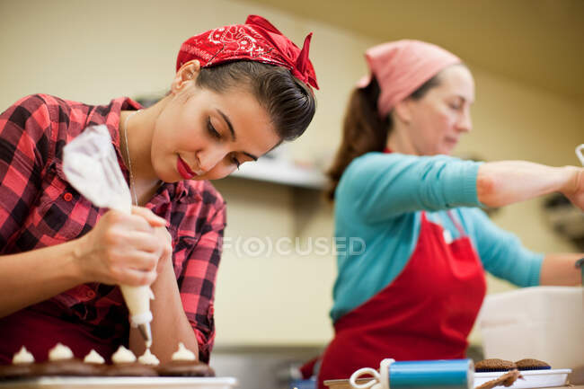 Giovane donna che utilizza borsa glassa in panetteria — Foto stock
