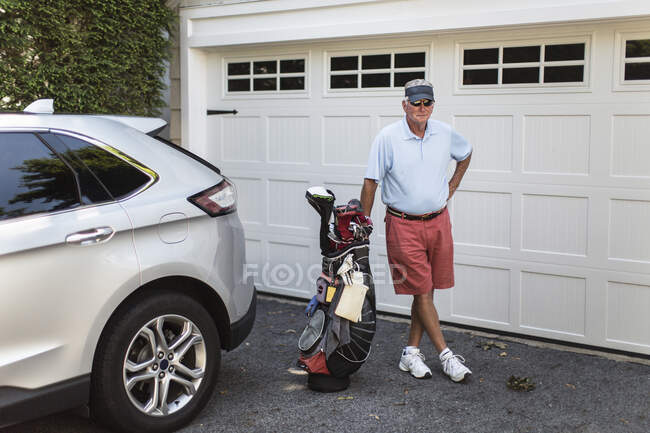 Portrait of man going golfing by his car and garage with his golfclubs — Stock Photo