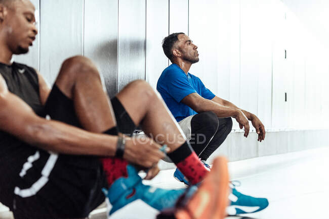 Exaustos jogadores de basquete masculino fazendo uma pausa no chão do vestiário — Fotografia de Stock