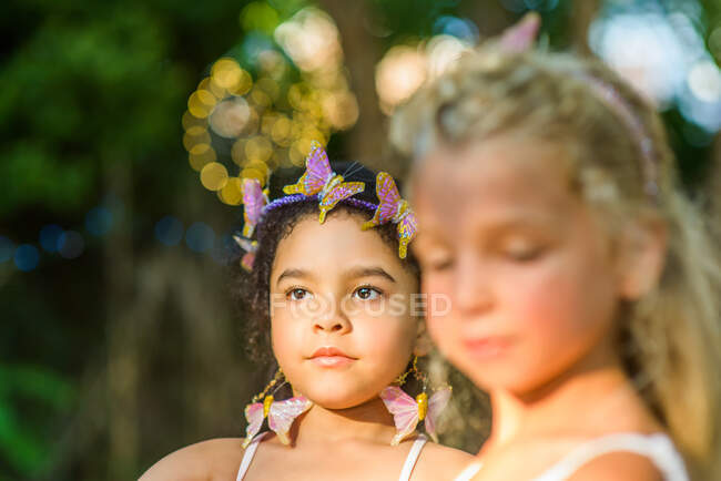 Two young girls, outdoors, wearing butterflies in hair — Stock Photo