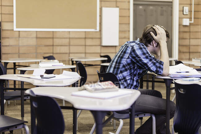 Fed up teenage boy with head in hands in high school classroom — Stock Photo