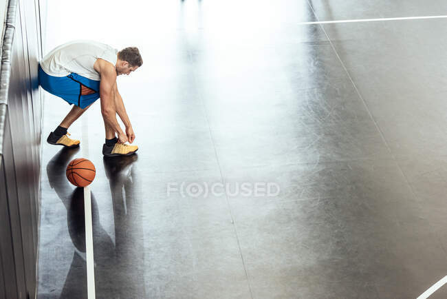 Jugador de baloncesto masculino atando cordones de entrenador en cancha de baloncesto - foto de stock