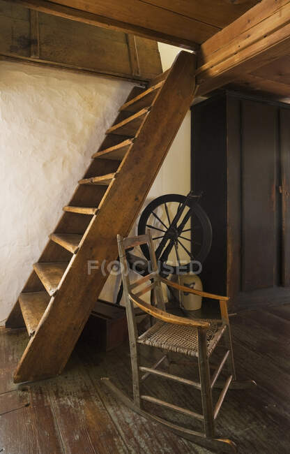 Старе дерев'яне крісло-гойдалка і прядіння колеса поруч зі сходами в спальні на верхньому поверсі, що веде до горища в старому (1785) стилі житлового будинку в стилі фелдстоун, Квебек, Канада. Це зображення звільняється власністю. CUPR0260 — стокове фото