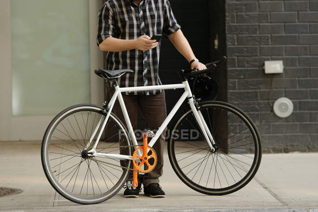 Neck down view of male cycle messenger checking directions on smartphone outside office — Stock Photo