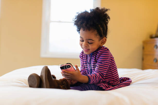 Fille jouer avec téléphone portable sur le lit — Photo de stock
