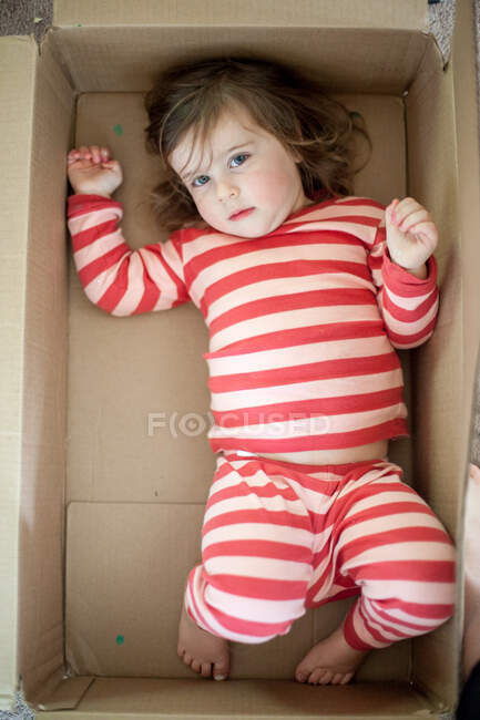 Девочка играет, лежа в коробке — стоковое фото