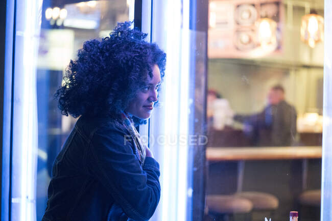 Woman looking through cafe window at night — Stock Photo