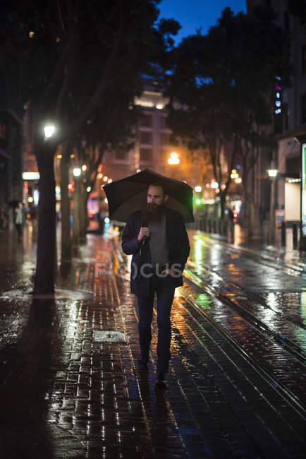 Мужчина, гуляющий по городу ночью, используя умбрехт, Центр города, Сан-Франциско, Калифорния, США — стоковое фото