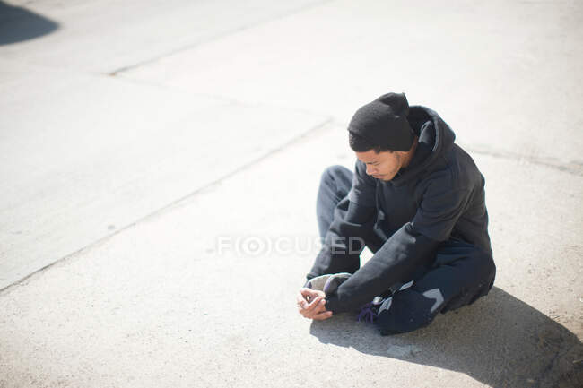 Hombre sentado en la acera, estirándose - foto de stock