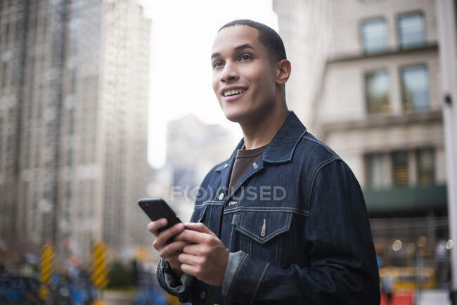 Joven parado en la calle, usando smartphone, Manhattan, Nueva York, EE.UU. - foto de stock