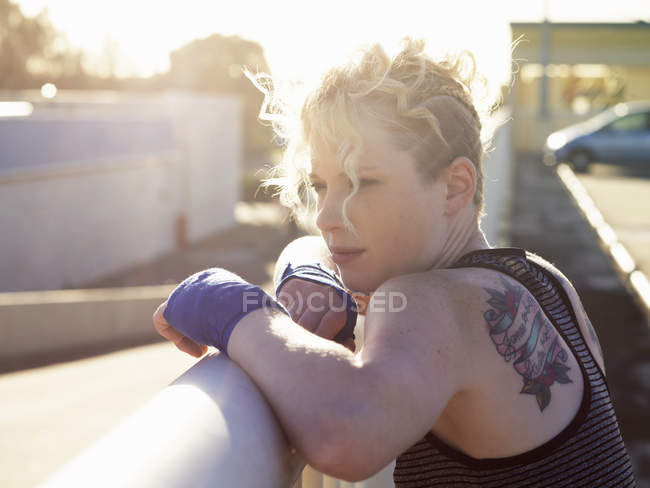 Portrait of young female boxer leaning against urban railing — Stock Photo