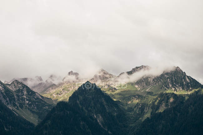 Скалистые горы с низкими облаками и освещенной солнцем долиной — стоковое фото