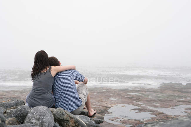 Rückansicht von Paar, das sich am felsigen Strand umarmt — Stockfoto