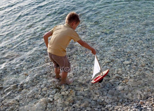 Menino com barco de brinquedo na praia — Fotografia de Stock