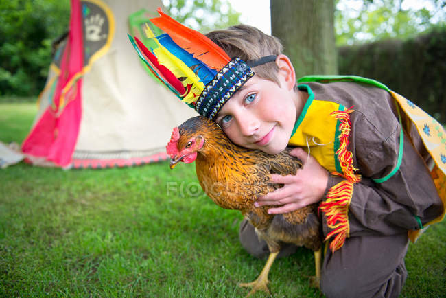 Boy dressed in Native American costume holding chicken, portrait — Stock Photo