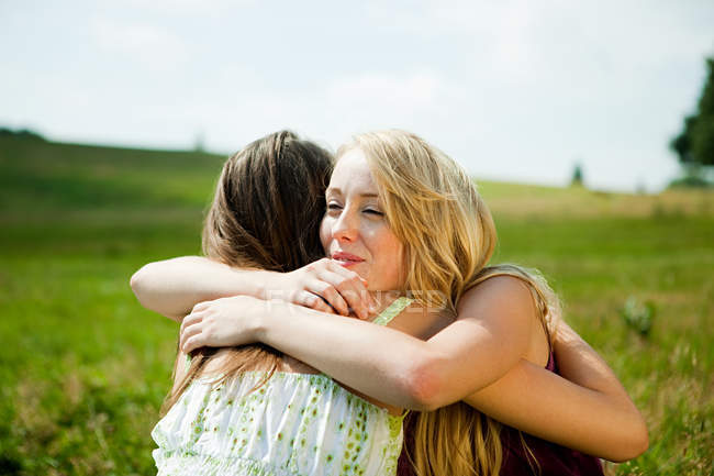 Mujeres jóvenes abrazándose en un campo - foto de stock