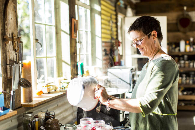 Woman pouring liquid into preserves jars in kitchen — Stock Photo