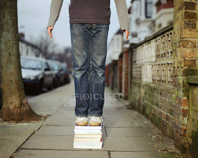 A young man standing on a pile of books — Stock Photo
