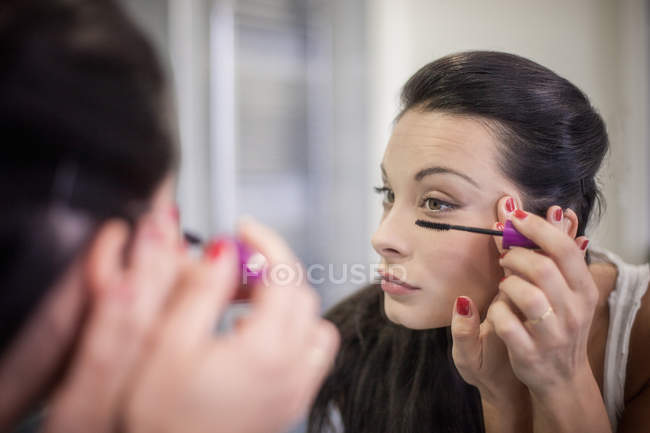 Over the shoulder mirror image of young woman applying mascara — Stock Photo