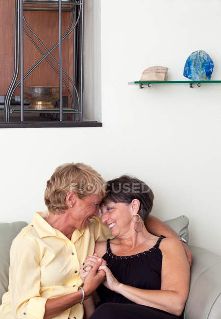 Mature lesbian couple embracing on sofa — Stock Photo