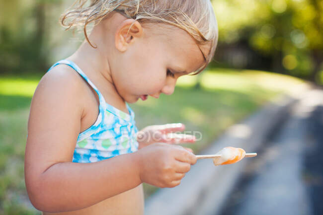 Girl with wet hair holding ice lolly, looking down — Stock Photo