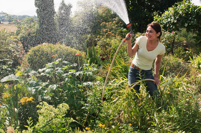 Mujer rociando jardín con manguera - foto de stock