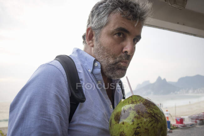 Hombre bebiendo jugo de coco fresco, Playa de Ipanema, Río de Janeiro, Brasil - foto de stock