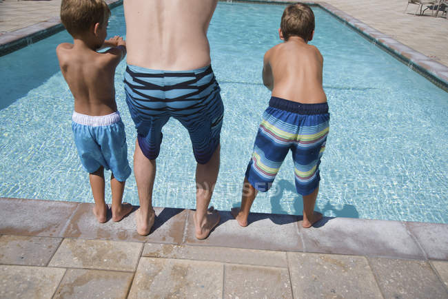 Rear view of man and two sons practicing diving poolside, Laguna Beach, California, USA — Stock Photo