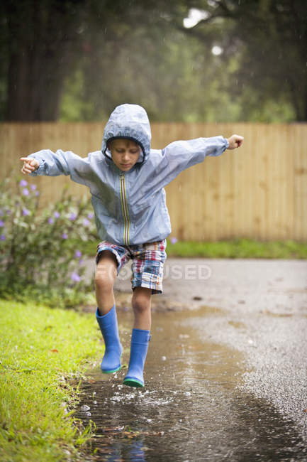 Хлопчик в гумових чоботях стрибає в дощовій калюжі — стокове фото