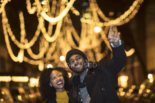 Romantic happy couple enjoying city during winter holidays looking at outdoor holiday lights — Stock Photo