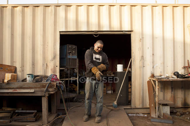 Construtor na frente do contêiner de transporte colocando luvas de proteção — Fotografia de Stock
