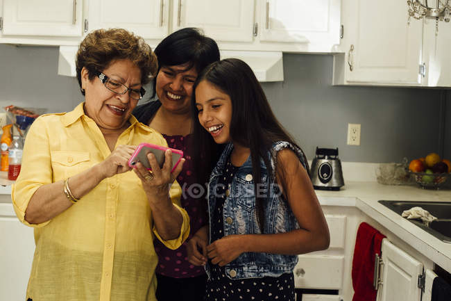 Семья из нескольких поколений смотрит на смартфон и улыбается — стоковое фото