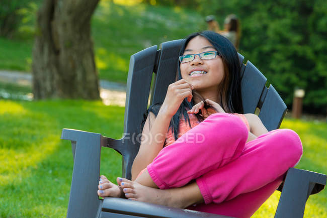 Дівчина сидить на садовому стільці, дивлячись геть усміхнений — стокове фото