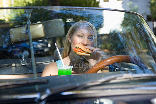 Woman eating hamburger in convertible — Stock Photo