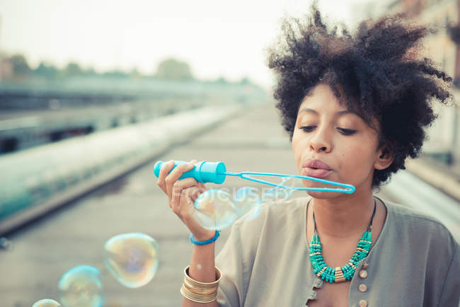 Jeune femme soufflant baguette à bulles en ville — Photo de stock