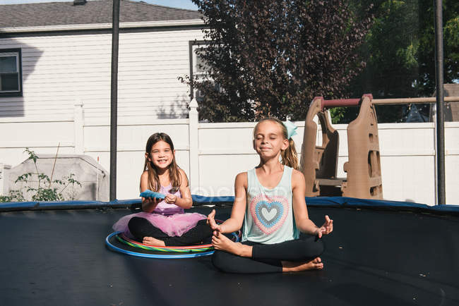 Meninas sentadas de pernas cruzadas no trampolim, meditando — Fotografia de Stock