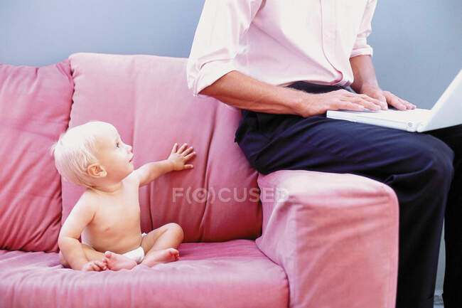 Baby on sofa with man typing — Stock Photo