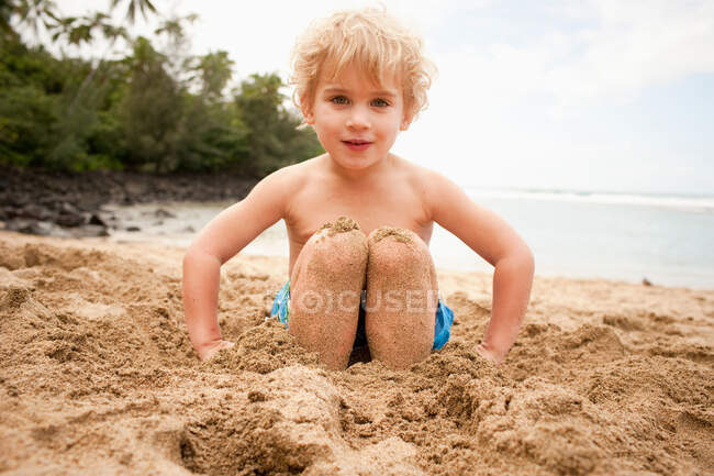Young boy with feet buried in sand on beach, portrait — Stock Photo