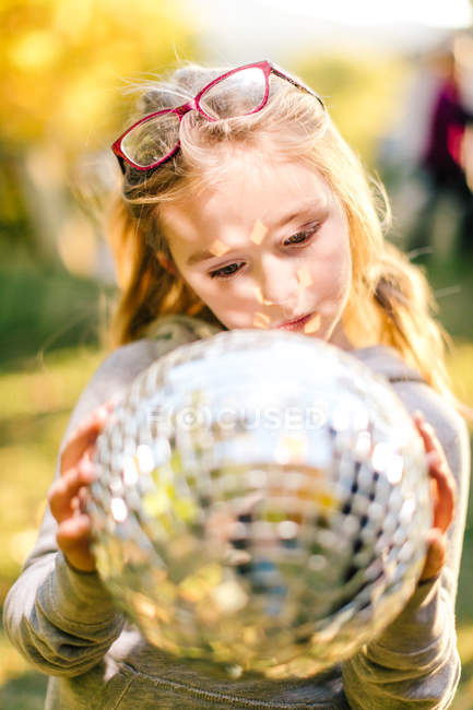 Girl in sunlit garden gazing at disco ball — Stock Photo