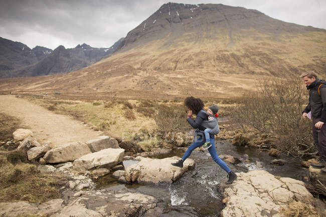 Mujer saltando sobre el arroyo, Piscinas de hadas, cerca de Glenbrittle, Isla de Skye, Hébridas, Escocia - foto de stock