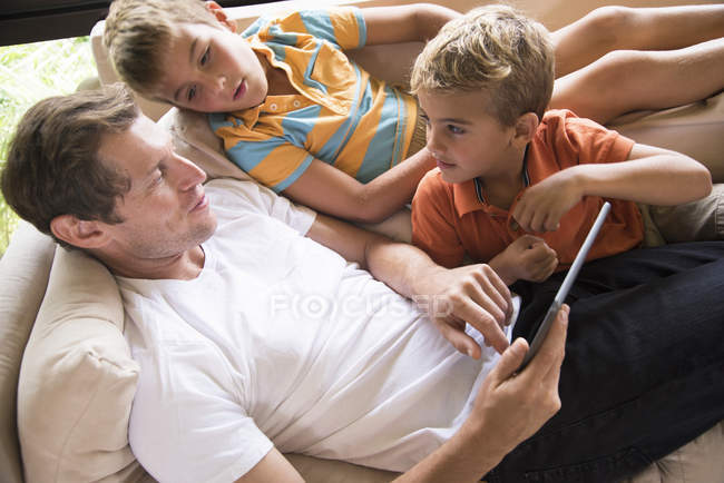 Мужчина и двое сыновей с цифровым планшетным сенсорным экраном на диване — стоковое фото