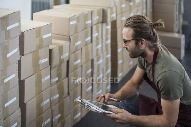 Mann checkt mit digitalem Tablet verpackte Produkte in Lagerraum der Fabrik — Stockfoto