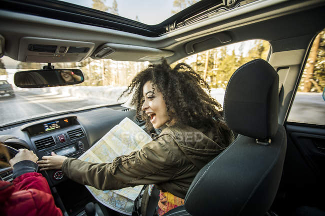 Mujer conduciendo coche, amigo en el asiento del pasajero mirando el mapa - foto de stock