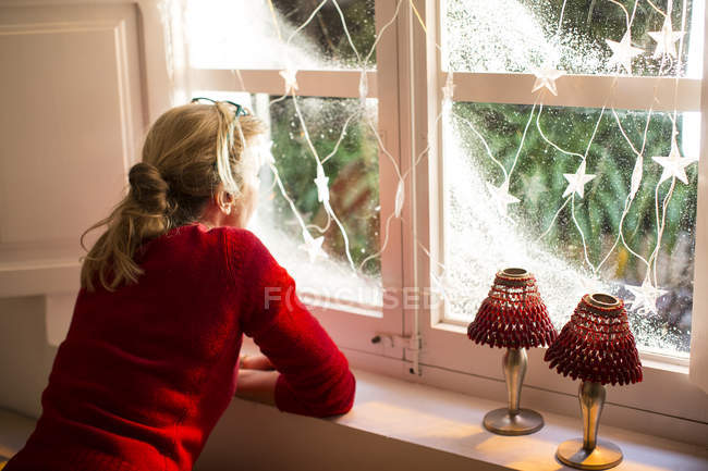 Женщина смотрит в окно с рождественскими украшениями — стоковое фото