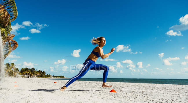 Молода жінка тренується, біжить між тренувальними шишками на пляжі — стокове фото