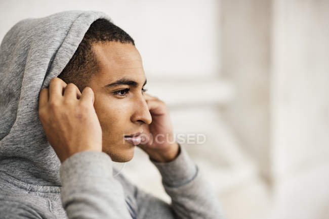 Corredor masculino vestindo capuz cinza colocando fones de ouvido — Fotografia de Stock