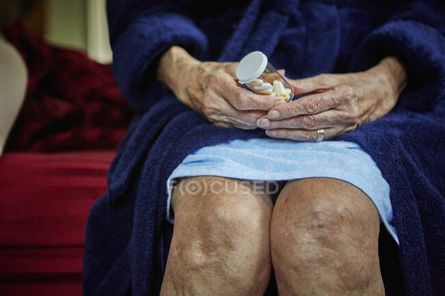 Старшая женщина сидит на краю кровати, держа бутылку с таблетками, средняя секция — стоковое фото