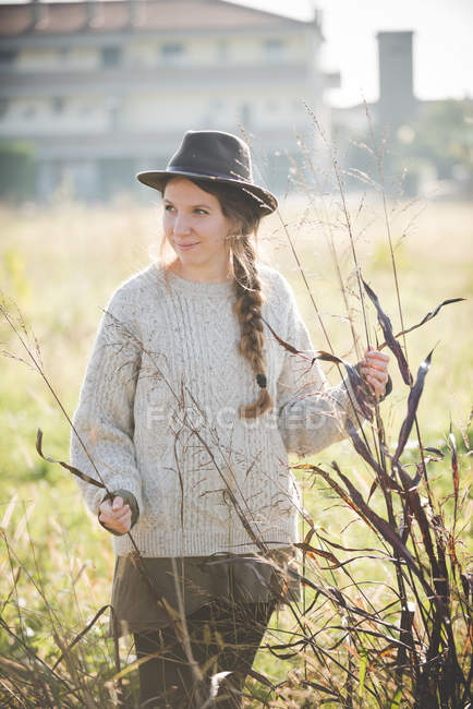 Молода жінка в капелюсі торкається рослин у полі — стокове фото